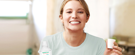 Žena se usmívá a drží ústní vodu a kelímek.